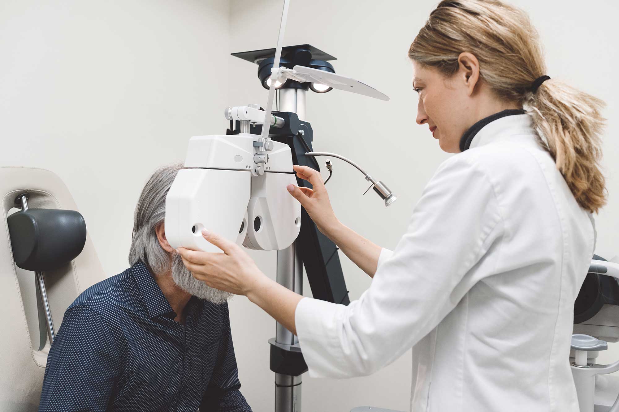 A woman closely examines an eye exam machine in a clinical setting, focusing on its features and functionality.