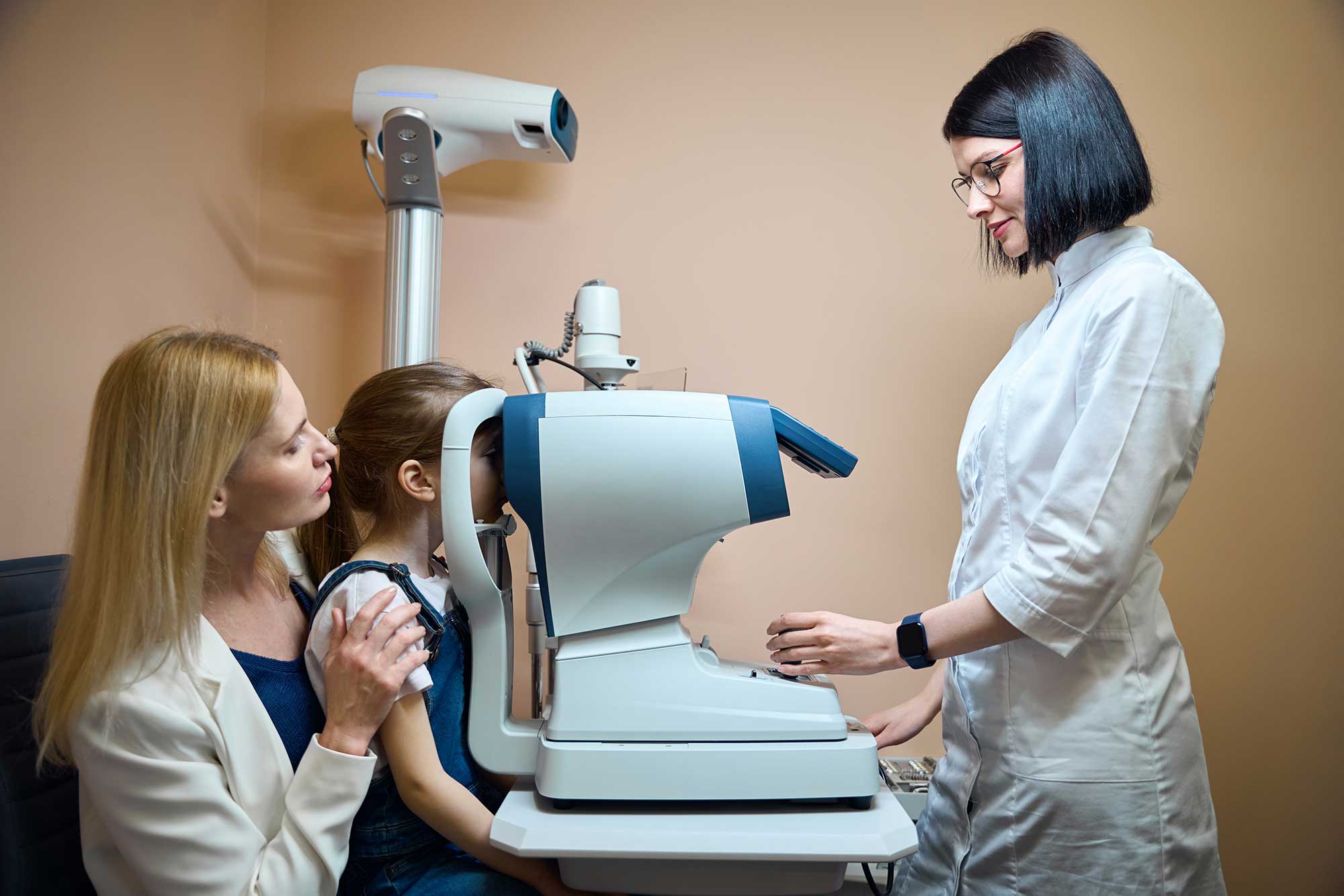 A woman examines an eye exam machine while two children observe her attentively.