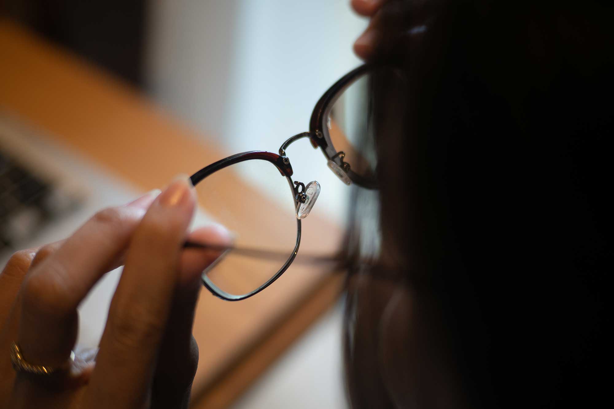 A woman examines her glasses while seated at a desk, focused on adjusting them for better clarity.