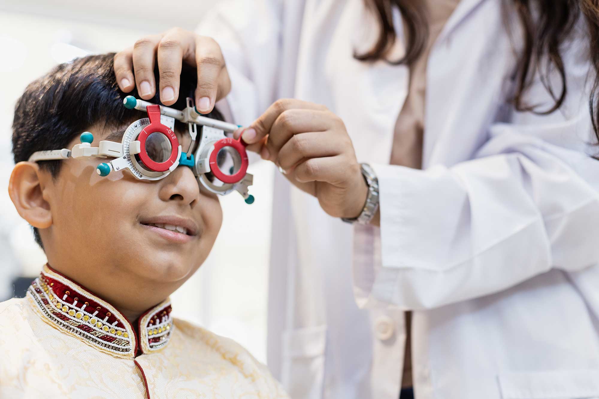 A young boy sits in an optometrist's chair while his eyes are being examined.